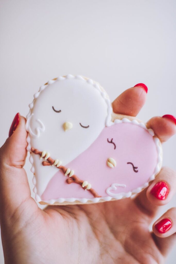Red-nailed hand holding a cute heart-shaped bird cookie.