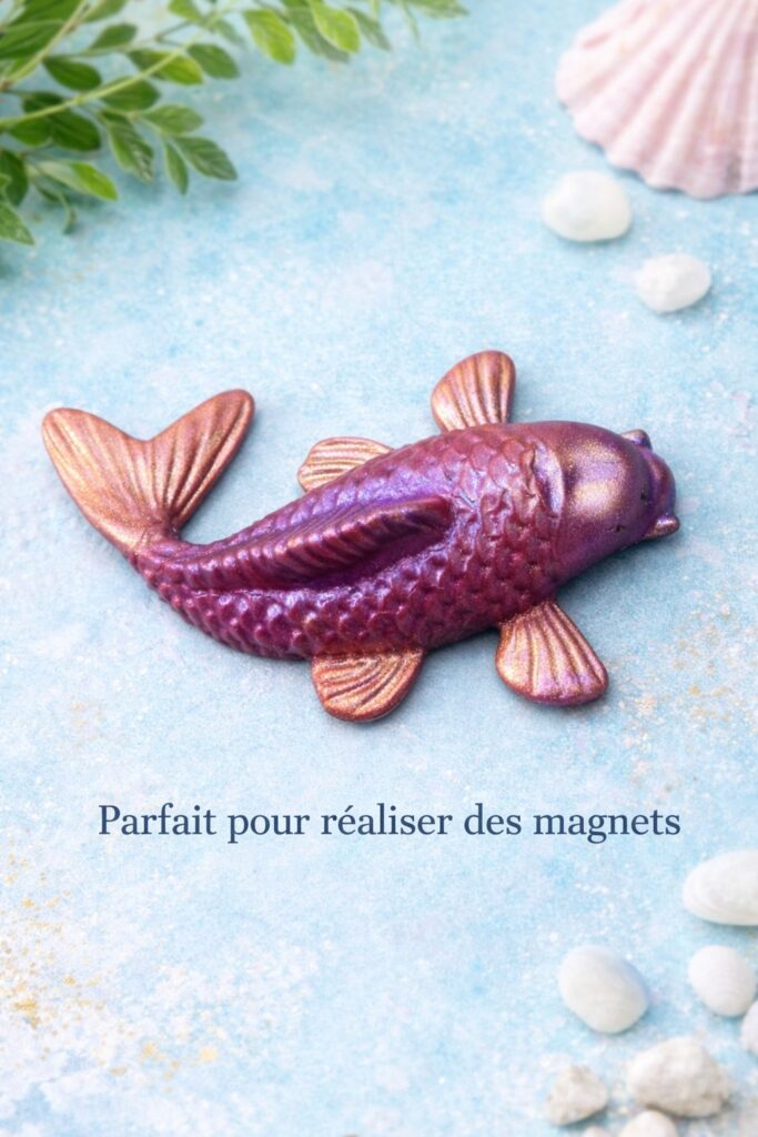 Poisson Koï en pâte polymère aux reflets irisés, réalisé avec des poudres de mica, posé sur un fond décoratif naturel, pouvant être utilisé pour la création de magnets