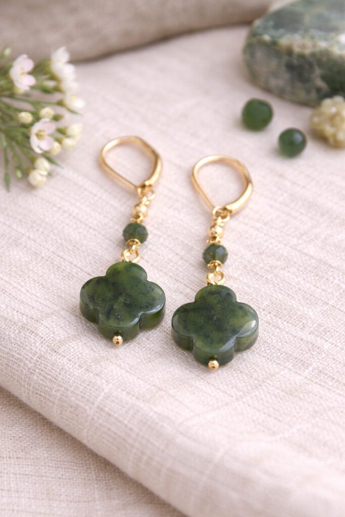 Paire de boucles d’oreilles artisanales composées de perles en jade néphrite du Canada sculptées en forme de trèfle. Les perles vert profond sont montées sur des apprêts dorés, avec de petites perles intermédiaires, et présentées sur un fond textile naturel. L’ensemble évoque une création de bijoux élégante, minimaliste et inspirée par les vertus symboliques de la pierre.